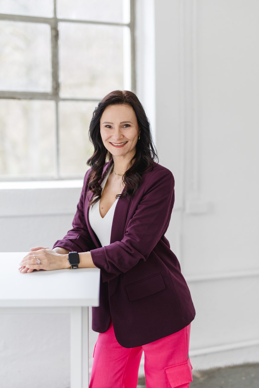 Karolina Dudek steht lächelnd am weißen Stehtisch vor einem hellen Fenster